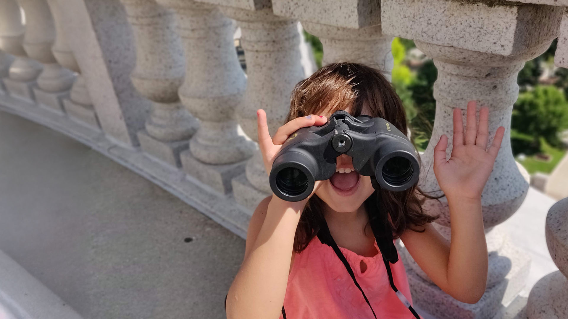 a small girl waves to the camera while looking through binoculars